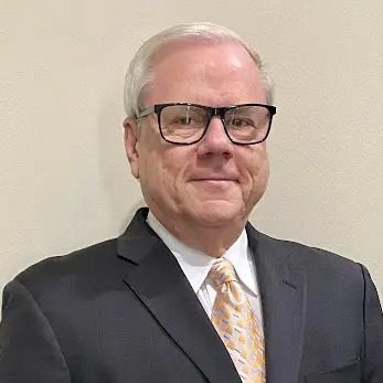 A man in suit and glasses standing next to wall.